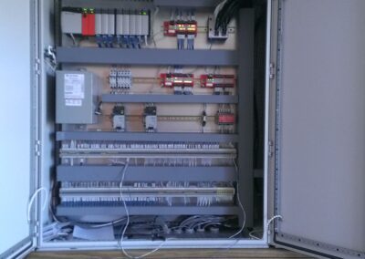 Open electrical cabinet with multiple rows of wiring, switches, and circuit components inside. Cables extend from the bottom.