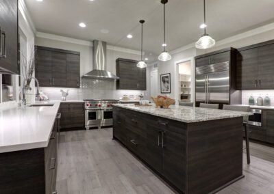 Modern kitchen with dark wood cabinets, marble countertops, and stainless steel appliances, including a range and refrigerator. Three pendant lights hang above a central island.